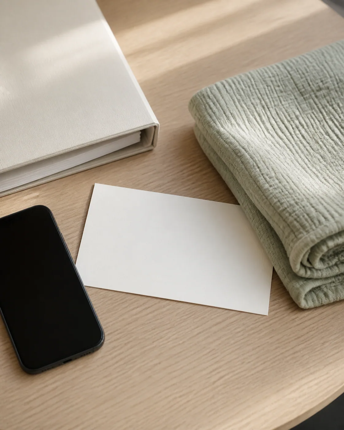 A blank guardian note, dark-screen phone, slim binder, and folded baby blanket on a pale table.